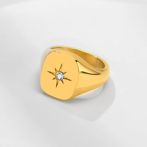 Detail of a gold signet ring featuring a starburst engraving and a central zircon stone