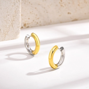 Close-up of two-tone gold and silver stainless steel hoop earrings on a stone surface