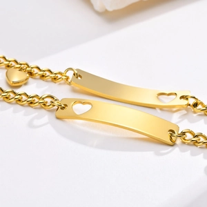 Detailed macro view of the gold heart cutout ID plate and dainty heart pendant on bracelet
