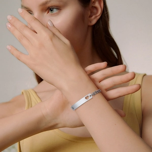 Detailed view of a silver heart engraved plaque bracelet on a model's wrist