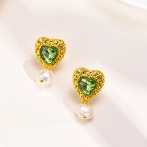 Gros plan sur les boucles d'oreilles cœur doré avec zircon vert et perle blanche