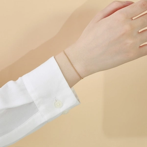 Détail d'un bracelet minimaliste en chaîne serpent dorée porté au poignet avec revers blanc
