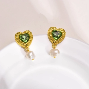 Détail de boucles d'oreilles cœur zircon vert et perles sur une assiette en céramique