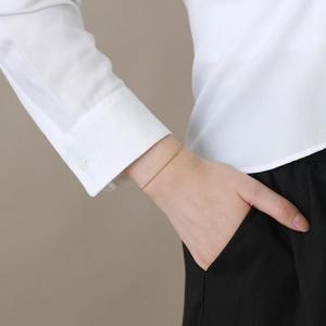 Bracelet chaîne serpent dorée minimaliste au poignet avec chemise blanche élégante