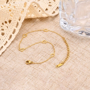 Gold stainless steel anklet with five hollow heart pendants on a textured beige backdrop