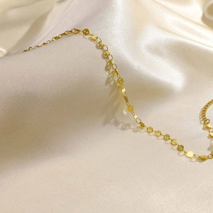 Detailed close-up of golden disc charm chain resting on champagne silk fabric surface