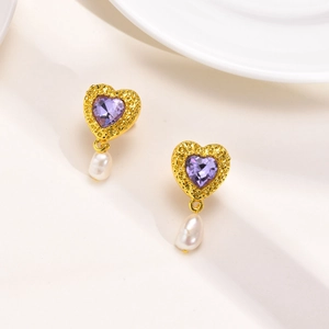 Détail de boucles d'oreilles cœur dorées avec cristal violet et perles baroques blanches