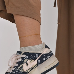 Close-up of a gold stainless steel anklet with hollow hearts on a model's ankle