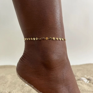 Close-up of minimalist gold layered anklet with disk charms on female model at the beach