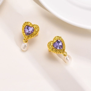 Gros plan sur des boucles d'oreilles cœur vintage dorées avec zircon violet et perle