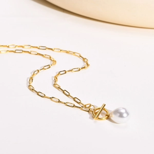 Gros plan d'un collier chaîne trombone doré avec perle ronde et fermoir à bascule