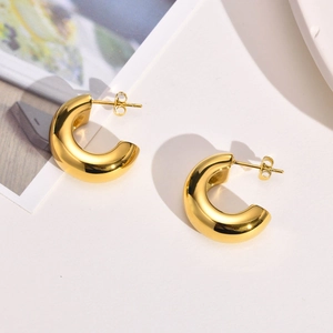 Detailed close-up of chunky gold C-shaped hoop earrings with a high-polished finish