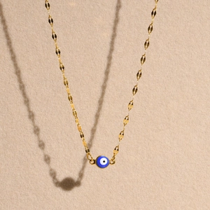 Detail of a gold-plated twisted chain necklace with a blue evil eye pendant on beige velvet