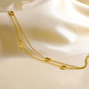 Close-up of a double-layered gold heart anklet on soft beige silk fabric background