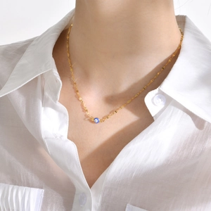 Detail of a gold evil eye pendant necklace worn on a neck with a white shirt