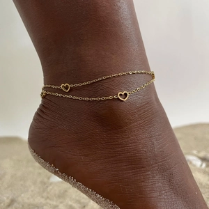Detailed view of a layered gold anklet with heart pendants on a beach setting