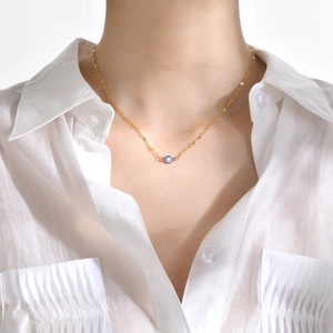 Close-up of golden evil eye pendant necklace worn on a white pleated shirt for women