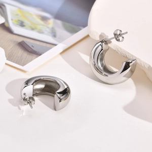 Detailed close-up of high-polished silver C-shaped hoop earrings on a stone surface