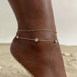 Detail of a golden double-layered anklet with three sparkling rhinestones on a beach