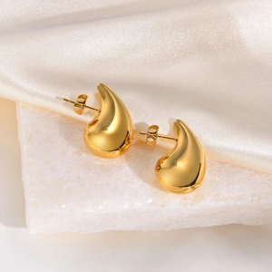 Close-up of golden teardrop earrings with mirror finish on white stone and silk background