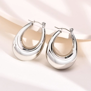Detailed close-up of chunky silver U-shape hoop earrings on white silk fabric background