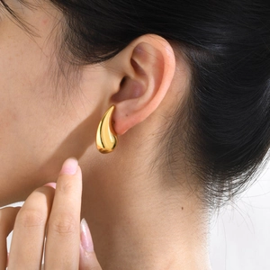 Macro view of polished gold teardrop earrings showing smooth metallic finish on skin