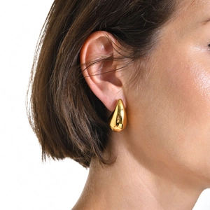 Close-up of a model wearing high-polished gold teardrop earrings in a minimalist style