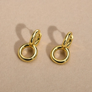 Polished gold double hoop earrings casting a heart shadow on beige velvet surface