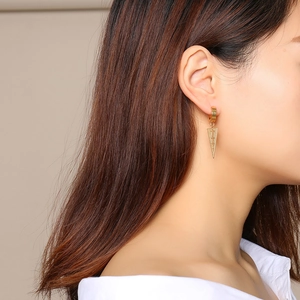 Close-up of a gold stainless steel hoop earring with an engraved cross on a conical charm