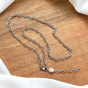 Detail of silver stainless steel chain with a natural white pearl on a wooden background