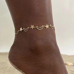 Detail of gold double-layer anklet with star and moon charms on sandy beach