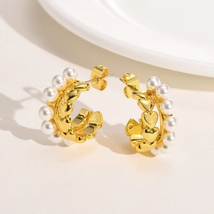 Détail de boucles d'oreilles créoles dorées avec perles blanches et motifs en cœur