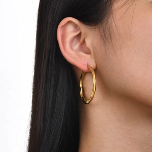 Close-up of model wearing large golden hammered textured hoop earrings for women