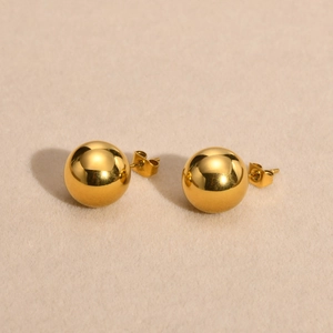 Boucles d'oreilles boules en acier inoxydable doré sur fond de sable beige