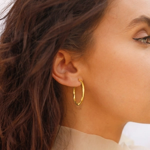 Golden stainless steel hoop earrings with hammered texture shown on female model