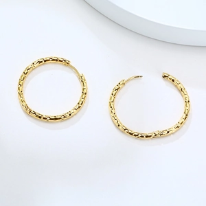 Détails macro des boucles d'oreilles créoles dorées en acier à texture martelée et fermoir