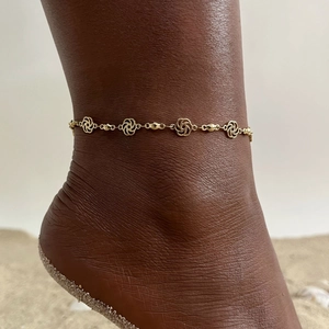 Close-up of golden stainless steel anklet with hollow flower charms on beach