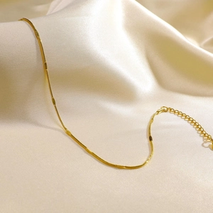 Close-up of golden double-layer snake chain anklet with flat metal accents on silk