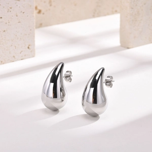 Macro detail of teardrop hollow stud earrings in polished silver on stone