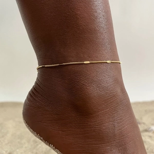 Detailed view of a gold double-layer stainless steel anklet on a beach background