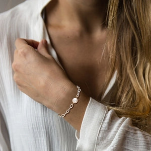 Detailed view of a silver flat oval link bracelet with a freshwater pearl and gold bead