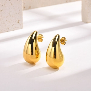 Macro detail of high-polish gold hollow teardrop earrings with butterfly backs on marble