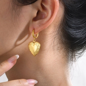 Detailed close-up of golden heart locket hoop earring with vintage floral engravings