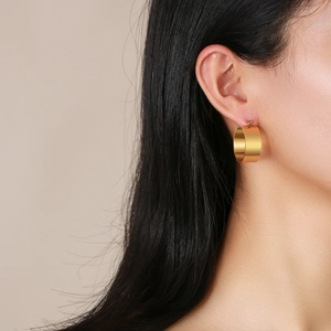 Polished gold stainless steel wide hoop earrings worn by a model in a side profile view