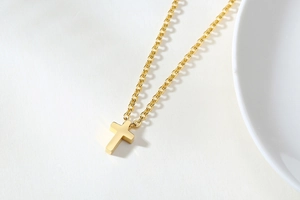 Detailed close-up of a polished gold cross pendant with fine link chain on white background
