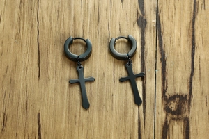 Detail of black stainless steel cross drop earrings with clicker closure on wood