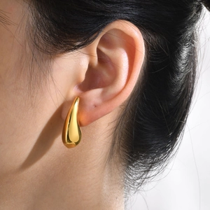 Macro detail of polished gold teardrop earring worn by model showing mirror-like finish