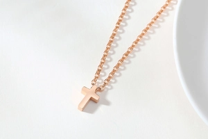 Close-up of minimalist rose gold cross pendant on a thin stainless steel chain