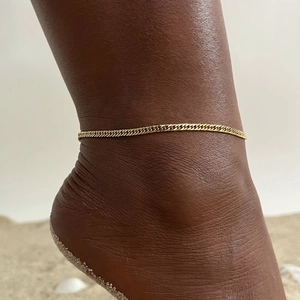 Detail of 18K gold-plated curb link anklet shown on skin against a beach background