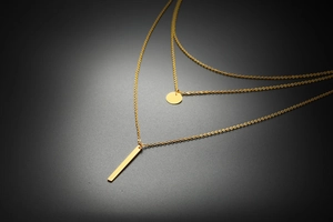 Détail macro du collier triple épaisseur doré avec pendentifs ronds et barrettes
